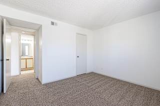 An empty bedroom in a model unit at Skyler Ridge Complex, with carpet flooring and a window for natural light.