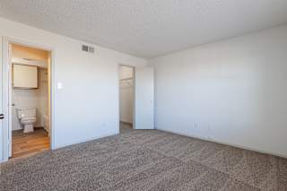 Empty model bedroom at Skyler Ridge with carpet, a ceiling fan, and an attached ensuite bathroom.
