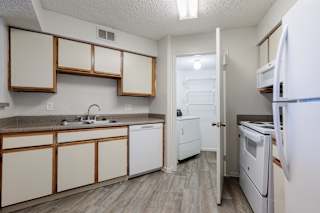 An empty kitchen in a model unit at Skyler Ridge Complex, featuring white appliances and wood cabinets.