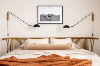 A bed with a white comforter and a brown blanket is in the foreground with a picture of a person riding a motorcycle hanging on the wall above it.