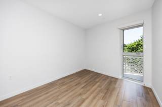 a living room with white walls and wood flooring and a door to a balcony