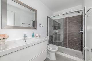 A white bathroom with a toilet, sink, mirror, and shower.