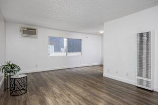 the living room and dining room of an apartment with white walls and wood floors