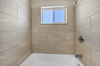 A white bathtub in a bathroom with a window above it.