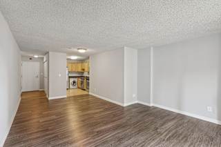 an empty living room and kitchen with wood flooring and white walls