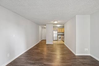the living room and kitchen of an apartment with white walls and wood floors