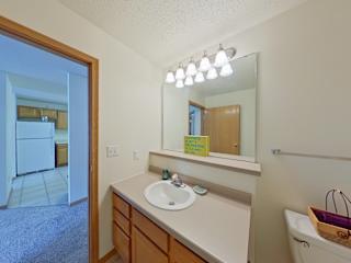A bathroom with a sink, mirror, and a basket on the tub.