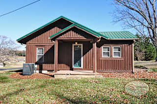 Side door to a rustic cabin style two bedroom home with a green roof.