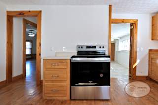 A kitchen with hardwood flooring, stainless steel stove top oven, and two door ways leading to the kitchen and laundry room.