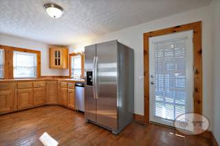 A kitchen with a stainless steel refrigerator, wooden cabinets, and hardwood flooring.