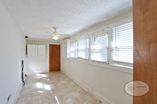 The large laundry room with white walls, vinyl flooring, ceiling fan, and a row of large windows.