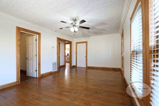 Living room with ceiling fan, hardwood flooring, and several doors.