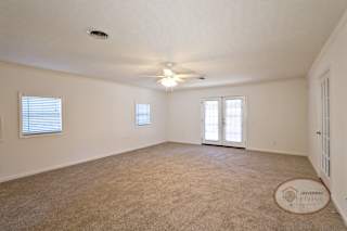 A spacious master bedroom with glass patio doors, carpet, and ceiling fan.
