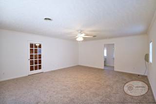 A spacious master bedroom with carpet, a glass door, and ceiling fan.
