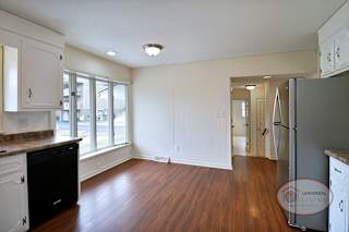 A kitchen with white cabinets, a large wall of windows, and hardwood floors.