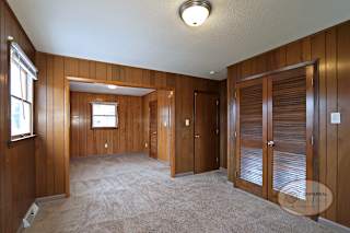 A room with wood paneling, closet, and catpet.