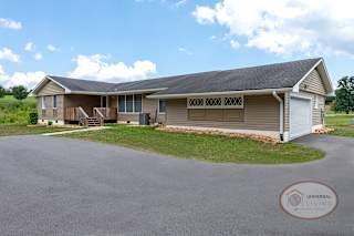 A tan house with dark roof, paved driveway and garage.