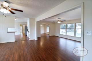 A spacious living area with dividing arch, hardwood floors, and ceiling fans.