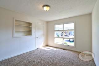 A bedroom with carpet, large decorative windows, and in wall shelves.