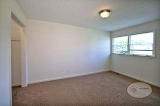 A bedroom with carpet, closet, and windows.