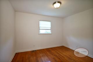 A bedroom with white walls, hardwood flooring, and a window.