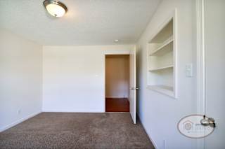 A bedroom with carpet, in wall shelves, and white walls.