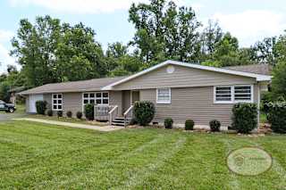 A grey house with attached garage in front of lush green trees.