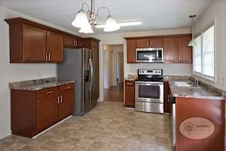 A kitchen with brown wooden  cabinets, stainless steel appliances, and tile floor.