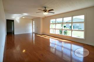 The living room with large decorate windows, hardwood floors, and ceiling fan.