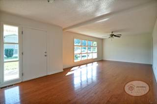 The living room with harwood floors, a ceiling fan, and very large decorative windows and plenty of natural light.