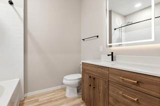 A white toilet sits in a bathroom with a white tub and a white sink.