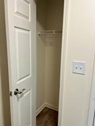 A white door with a silver handle is open to a small closet with a white shelf.