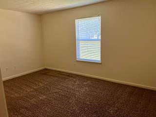 A room with a carpeted floor and a window with blinds.