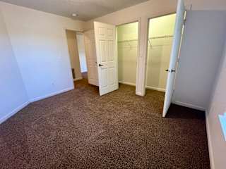 a bedroom with a carpeted floor and three closet doors at Shenandoah Properties in Lafayette, IN 47905