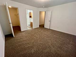 an empty living room with carpeting and a door to a bathroom at Shenandoah Properties in Lafayette, IN 47905