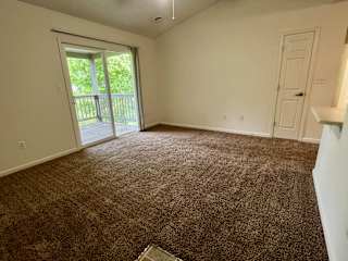 an empty living room with carpet and a door to a balcony at Shenandoah Properties in Lafayette, IN 47905