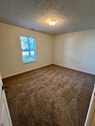 an empty living room with carpet and a window at Shenandoah Properties in Lafayette, IN 47905