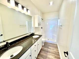 A bathroom with a sink, mirror, and wood flooring.