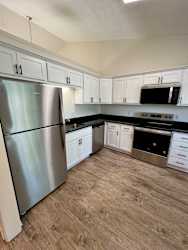 A kitchen with a stainless steel refrigerator and black countertops.