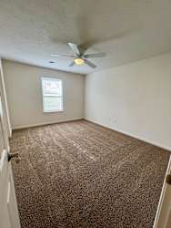 A room with a carpeted floor and a ceiling fan.