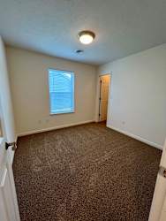 A room with a carpeted floor and a window with blinds.