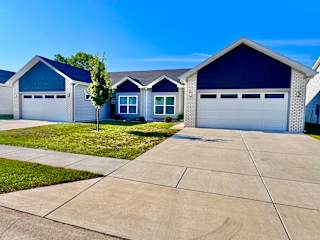 A blue house with a white garage door is in front of a green tree.