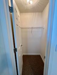 A small, white closet with a carpeted floor and a metal rack.
