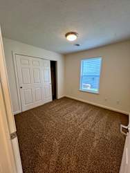 A room with a carpeted floor and a window with blinds.