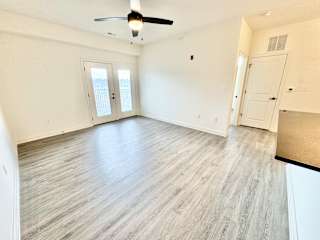 A room with a ceiling fan and light fixture, two doors, and a wooden floor.
