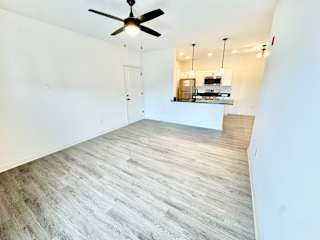 A room with a ceiling fan and a kitchen area in the background.