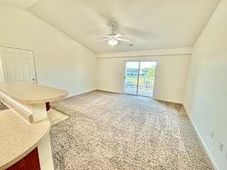 Cypress Upstairs Vaulted Living Room with Fan and Carpeted Floors, Glass Sliding Patio Door to Balcony at Hawthorne Properties in Lafayette, IN 47905