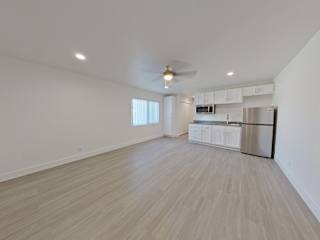 an empty living room with a ceiling fan and a kitchen in the background