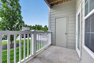 A white fence on a patio with a grey house and a tree in the background.