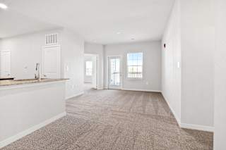 the living room and kitchen of an apartment with white walls and carpet  at Aventura at Hawk Ridge, Lake St Louis, 63367